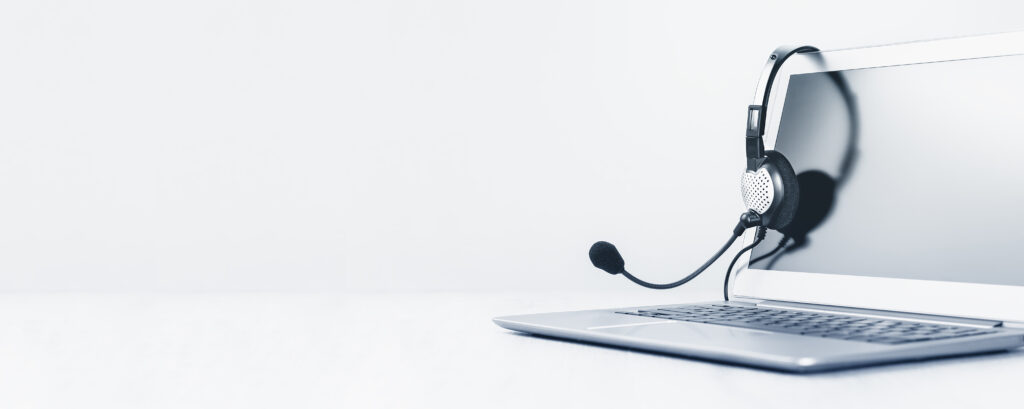 Laptop. Mockup screen and headphones on grey desk and plain background wide banner. Distant learning or working from home, online courses or support minimal concept. Helpdesk or call center headset